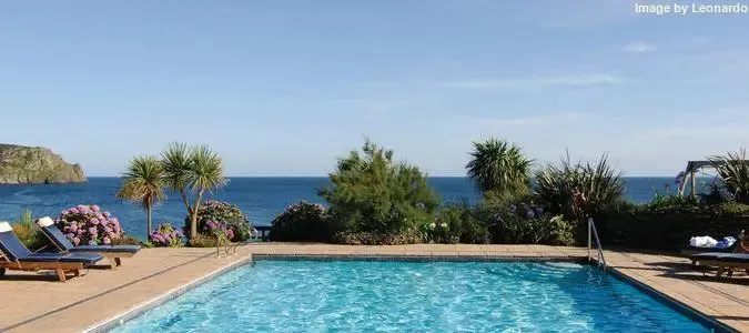 Une piscine bleue bordée de transats et de végétation luxuriante offre une vue sur la mer.