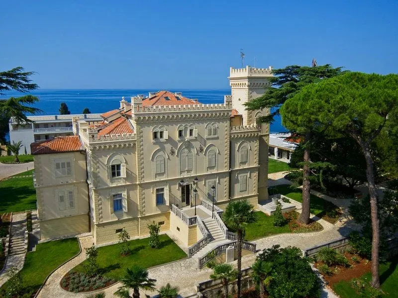 Bâtiment de style ancien avec jardin verdoyant et vue sur la mer.