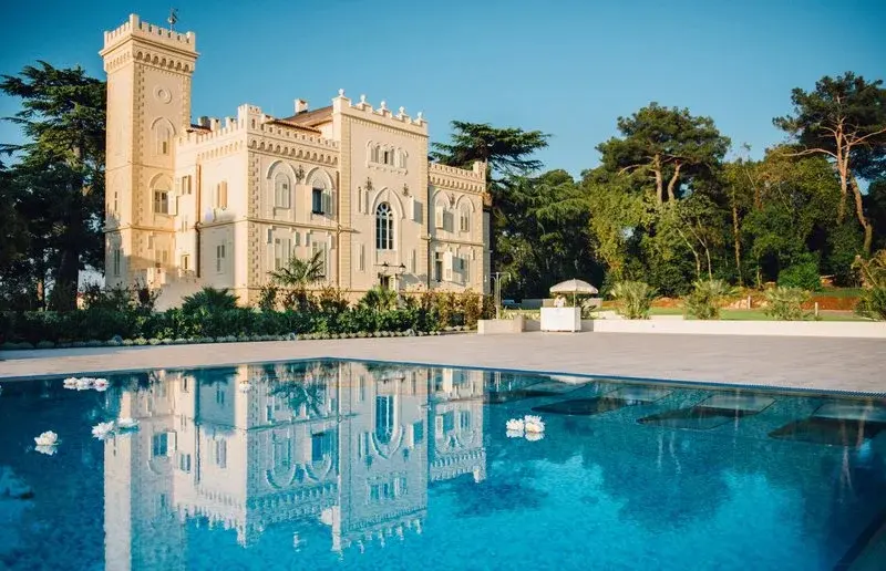 Bâtiment de style château se reflétant dans une piscine au bord d'une terrasse.