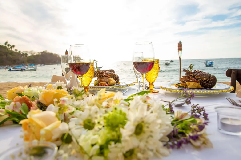 Une table dressée en bord de mer présente des plats décorés et des verres de vin.