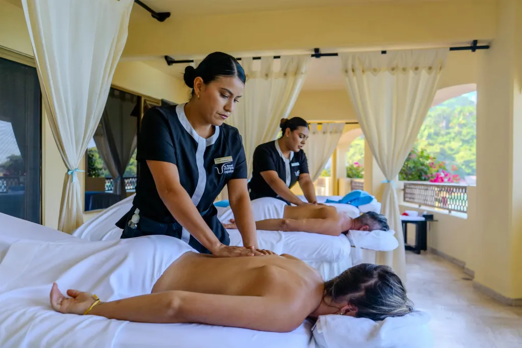 Deux personnes allongées reçoivent un massage dans un espace extérieur ombragé.
