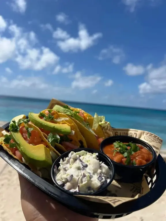 Assiette de tacos garnis avec accompagnements, vue sur la mer et le ciel nuageux.