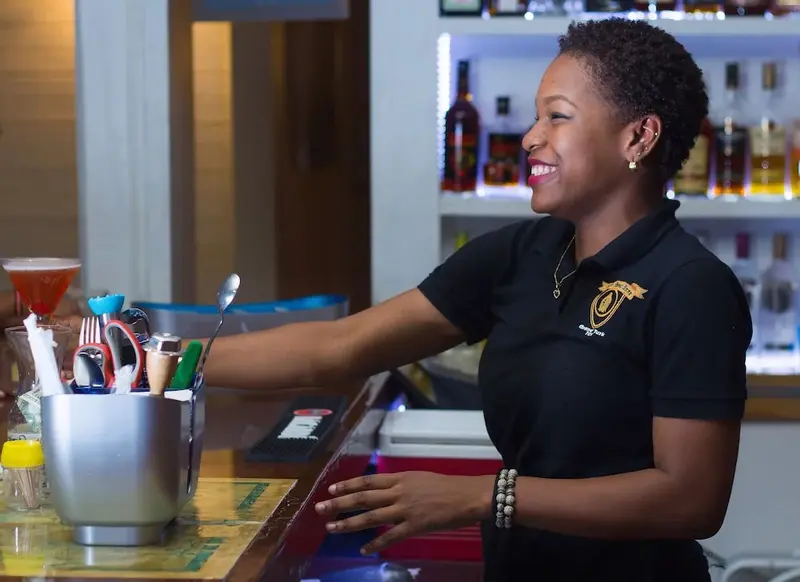 Une employée souriante se tient derrière un comptoir de bar bien garni.