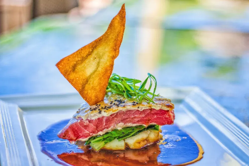 Assiette de poisson cru décorée d'une chips et de verdure.