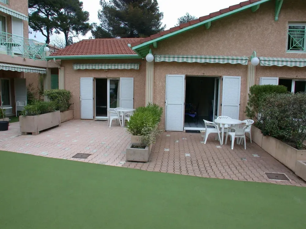 Terrasse pavée avec tables et chaises devant des logements aux volets clos.