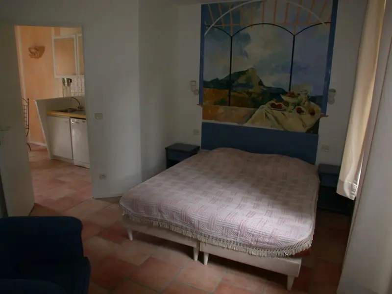 Une chambre lumineuse avec un lit et un coin cuisine attenant.