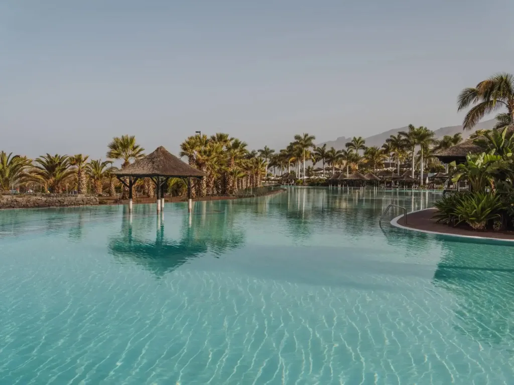 Une grande piscine turquoise bordée de végétation luxuriante et de structures ombragées.