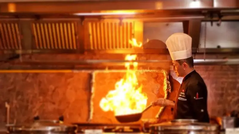 Un chef prépare un plat en flammant à la poêle dans une cuisine professionnelle.