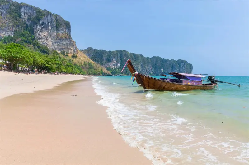 Une plage de sable fin borde une mer turquoise, avec un bateau traditionnel échoué sur le rivage.