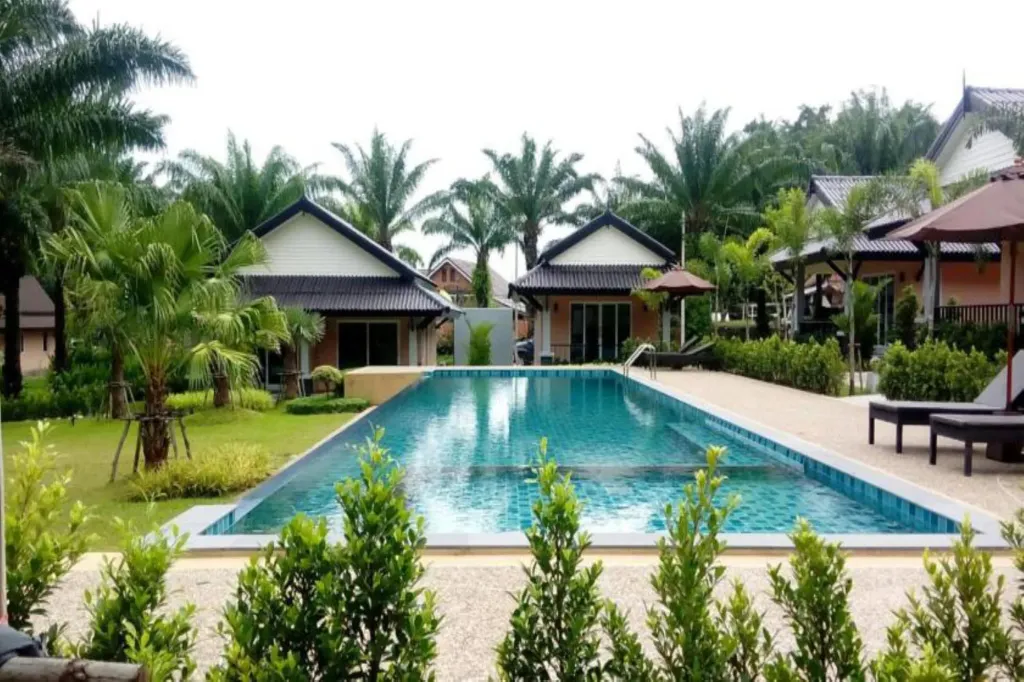 Une piscine rectangulaire bordée de transats et de végétation luxuriante.