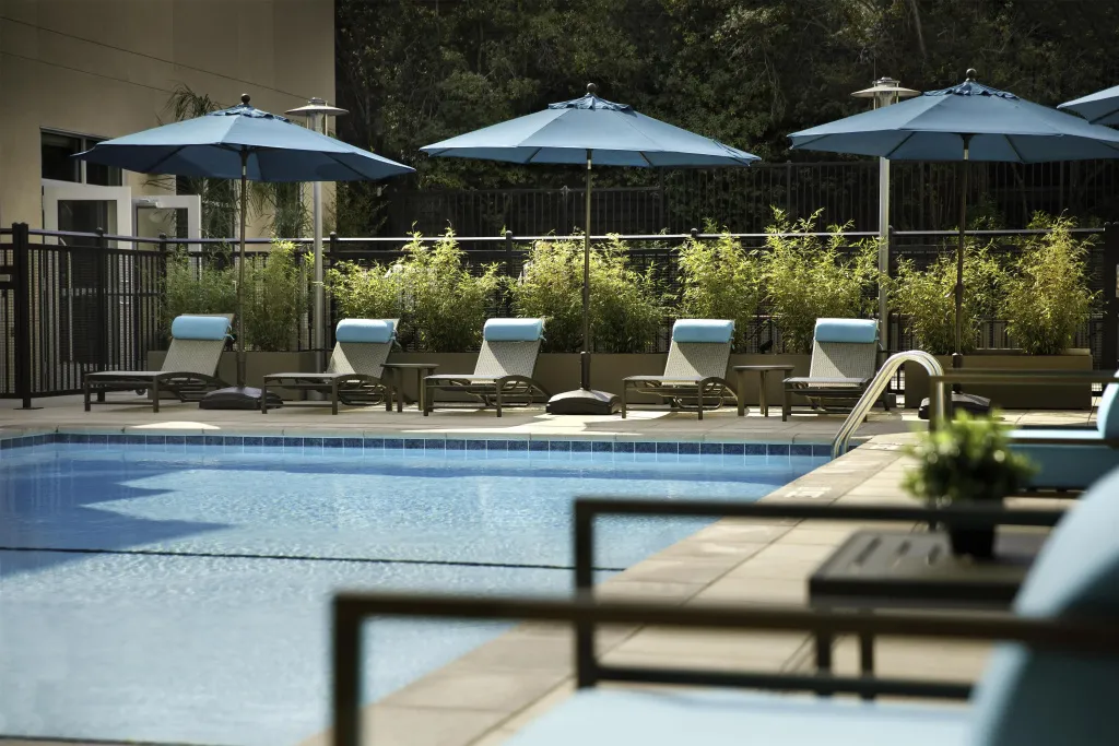 Transats bleus disposés au bord d'une piscine ensoleillée, protégés par des parasols.