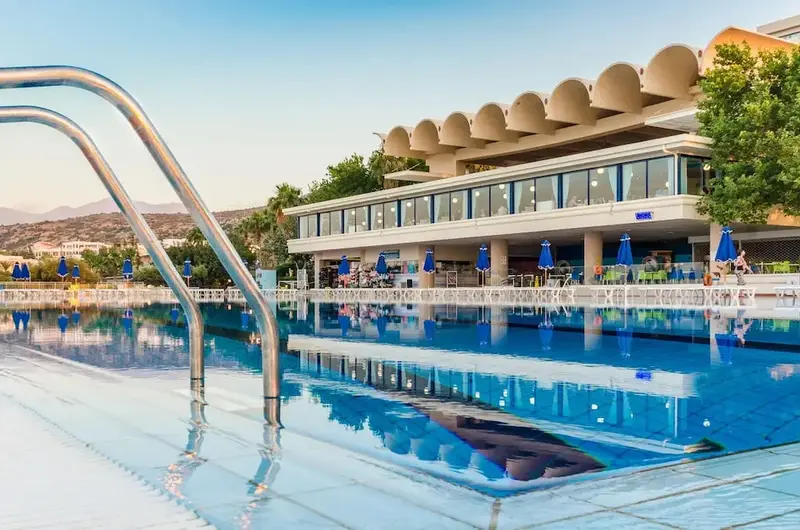 Une piscine bleu clair reflète un bâtiment moderne avec de larges baies vitrées.