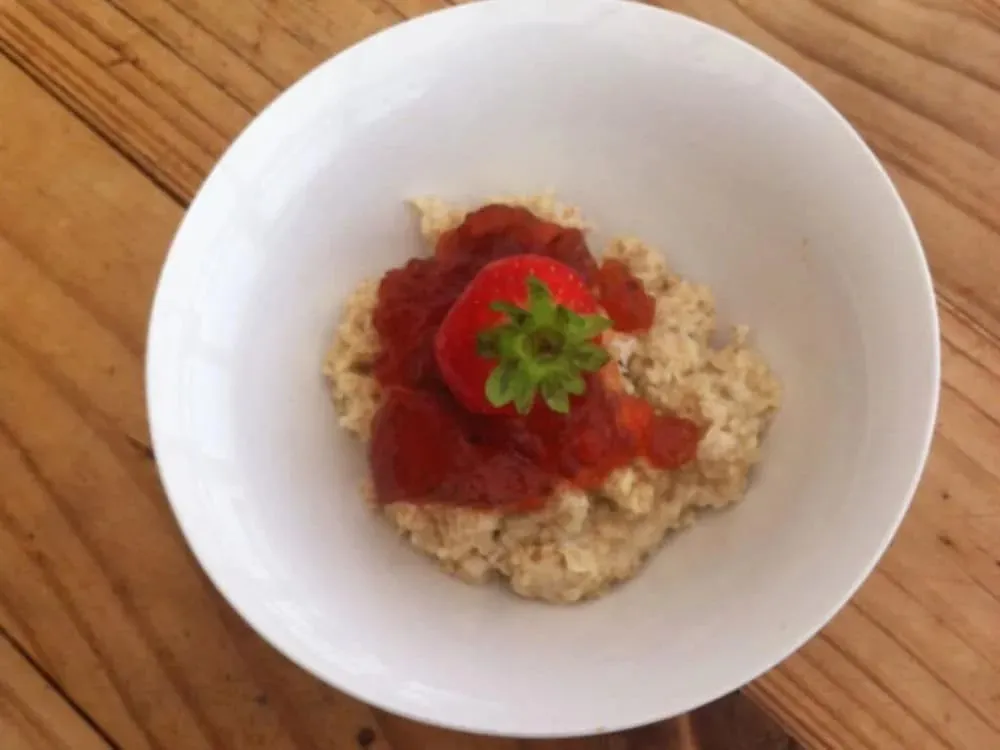 Un bol de céréales garni de fraises coupées et d'une fraise entière.