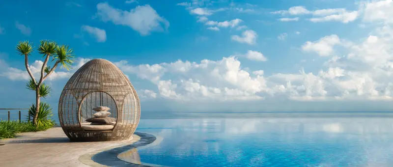 Une structure en osier abrite des coussins près d'une piscine à débordement.