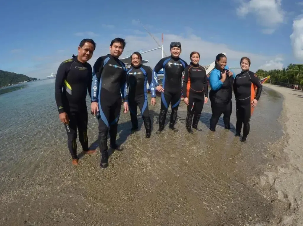 Groupe de personnes en combinaisons de plongée sur une plage de sable.