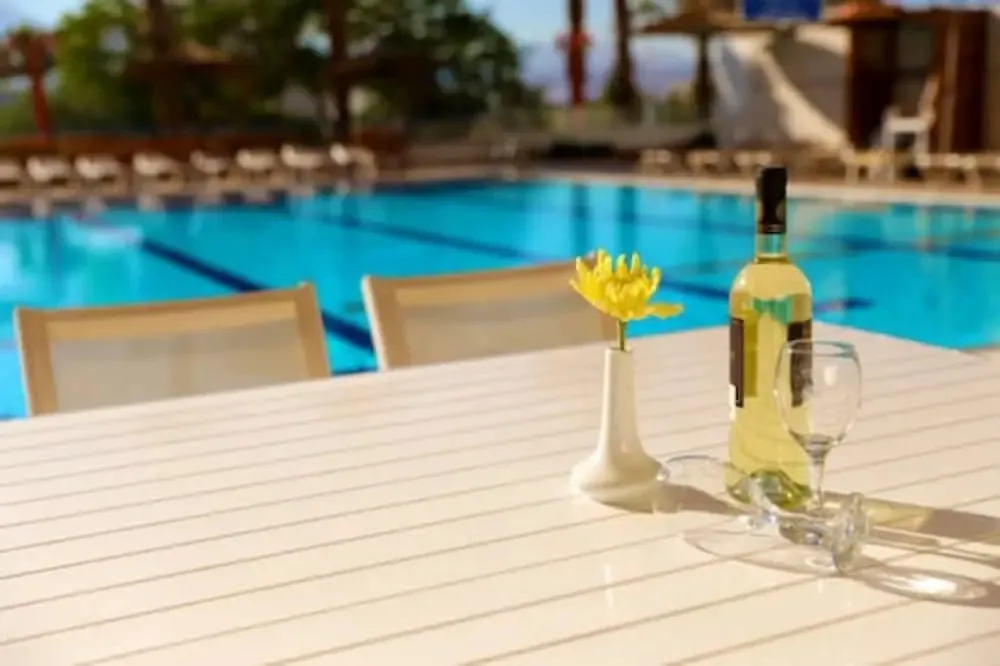 Une table avec une bouteille et un verre près d'une piscine ensoleillée.