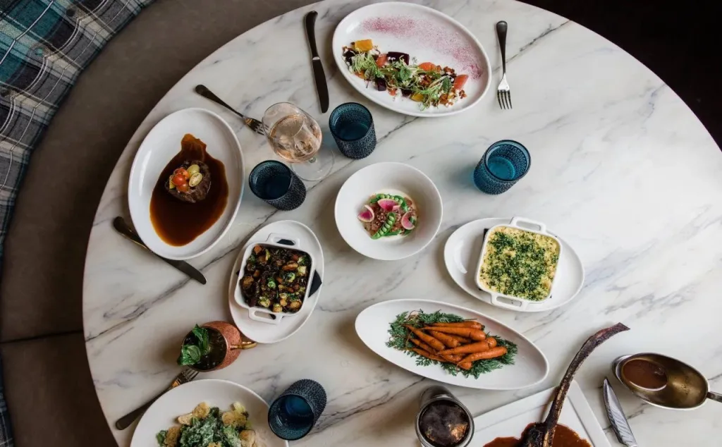 Une table ronde est dressée avec une variété de plats colorés et de boissons.