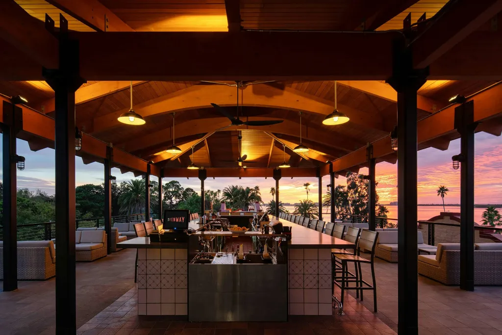 Un long comptoir de bar en plein air s'ouvre sur un coucher de soleil tropical.
