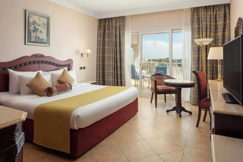 Une chambre lumineuse avec un grand lit et un coin repas près d'une baie vitrée.