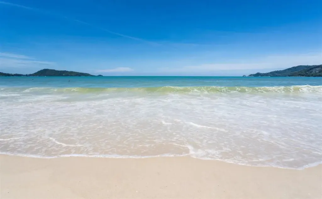 Vague déferlant sur une plage de sable fin sous un ciel bleu.