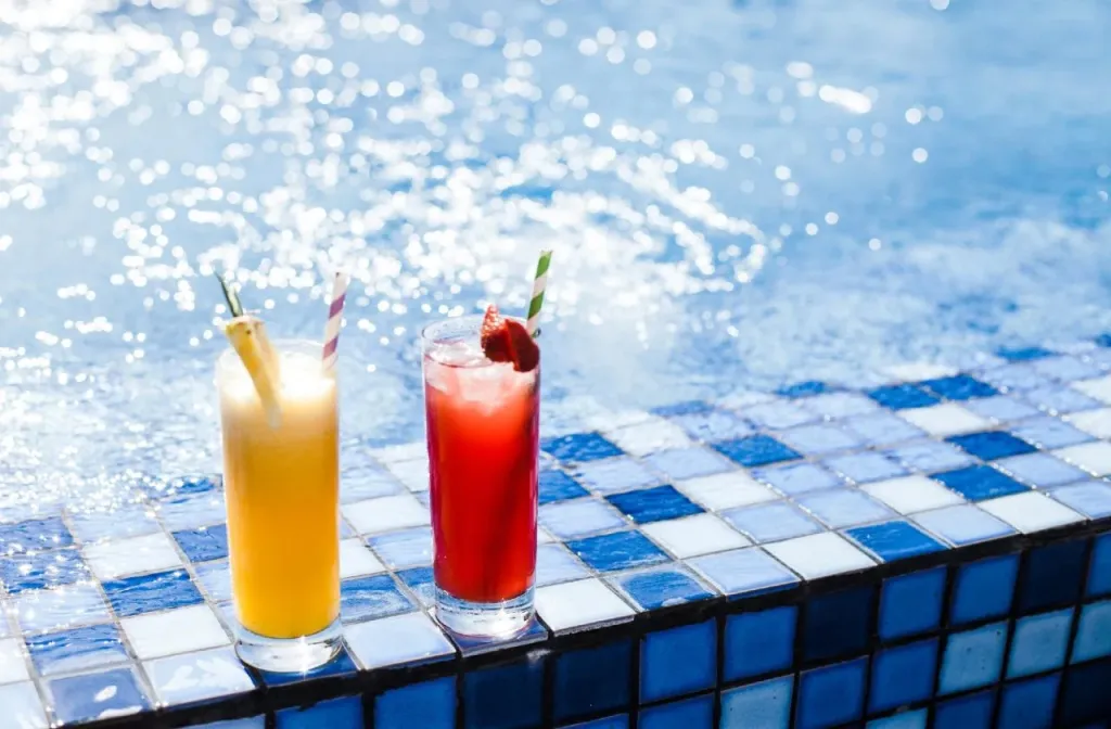 Deux cocktails colorés reposent sur le bord d'une piscine scintillante.