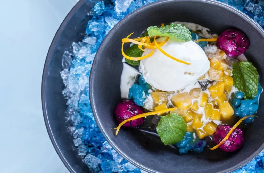 Une coupe de dessert à la glace, aux fruits et à la menthe est présentée sur un lit de glace pilée.