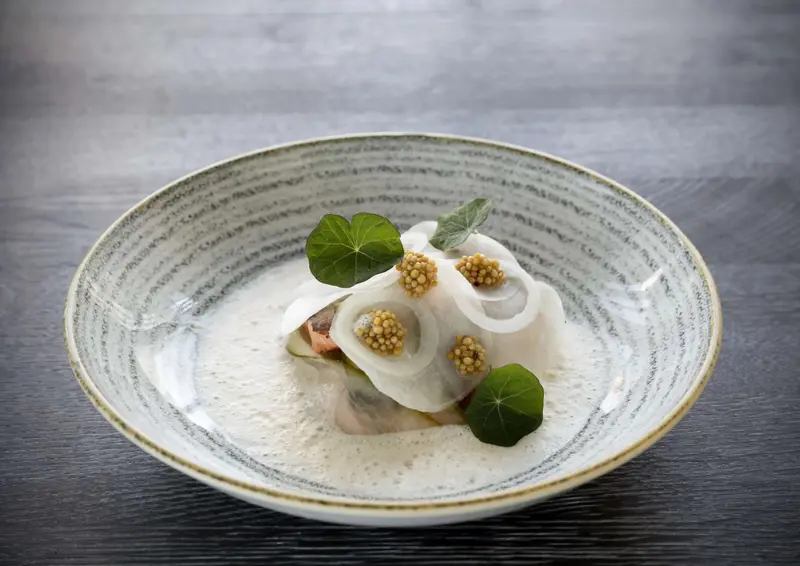 Un plat raffiné est présenté dans une assiette texturée sur une table en bois sombre.
