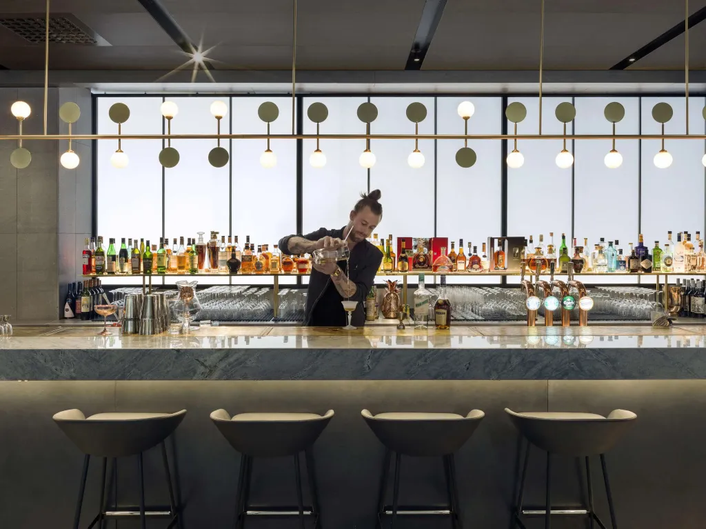 Un barman prépare un cocktail derrière un comptoir bien garni de bouteilles.