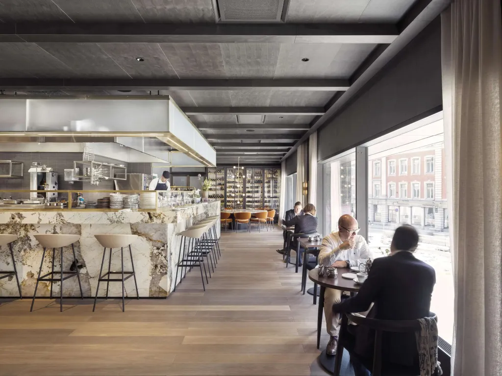 Une salle de restaurant lumineuse avec des clients attablés et un comptoir de bar en marbre.