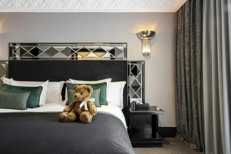 Un lit est fait dans une chambre décorée avec des oreillers et un ours en peluche.