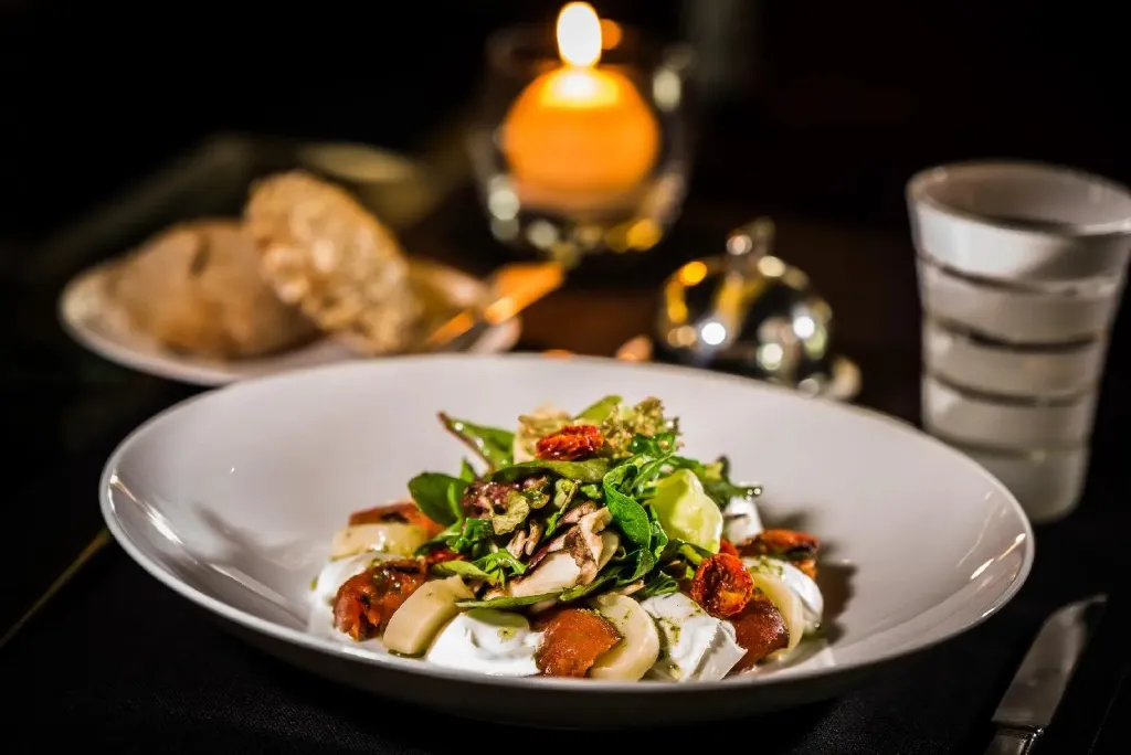 Assiette de salade colorée avec des tomates séchées et de la roquette, accompagnée de pain et d'une bougie.