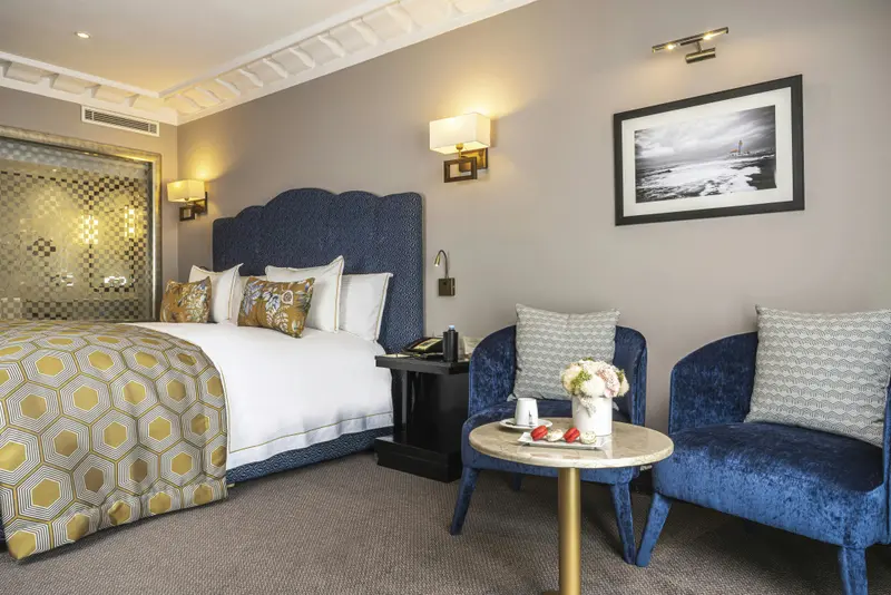 Une chambre d'hôtel lumineuse avec un grand lit et deux fauteuils.