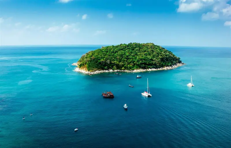 Vue aérienne d'une île tropicale entourée d'une mer turquoise et de plusieurs bateaux à voile.
