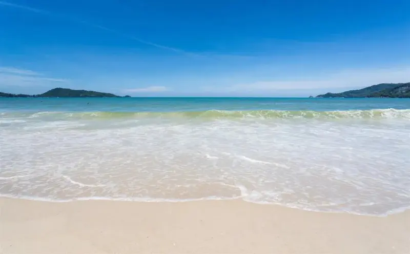 Vagues déferlant sur une plage de sable fin sous un ciel bleu.