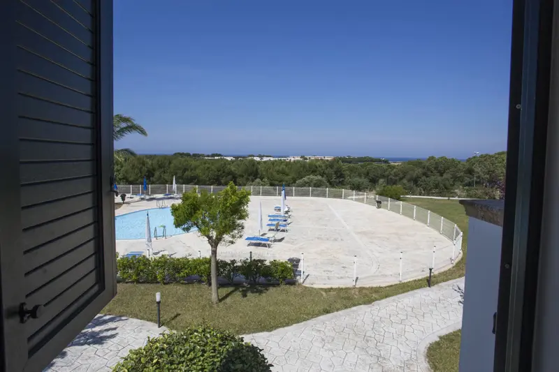 Vue sur une piscine et un terrain de beach-volley depuis une fenêtre.