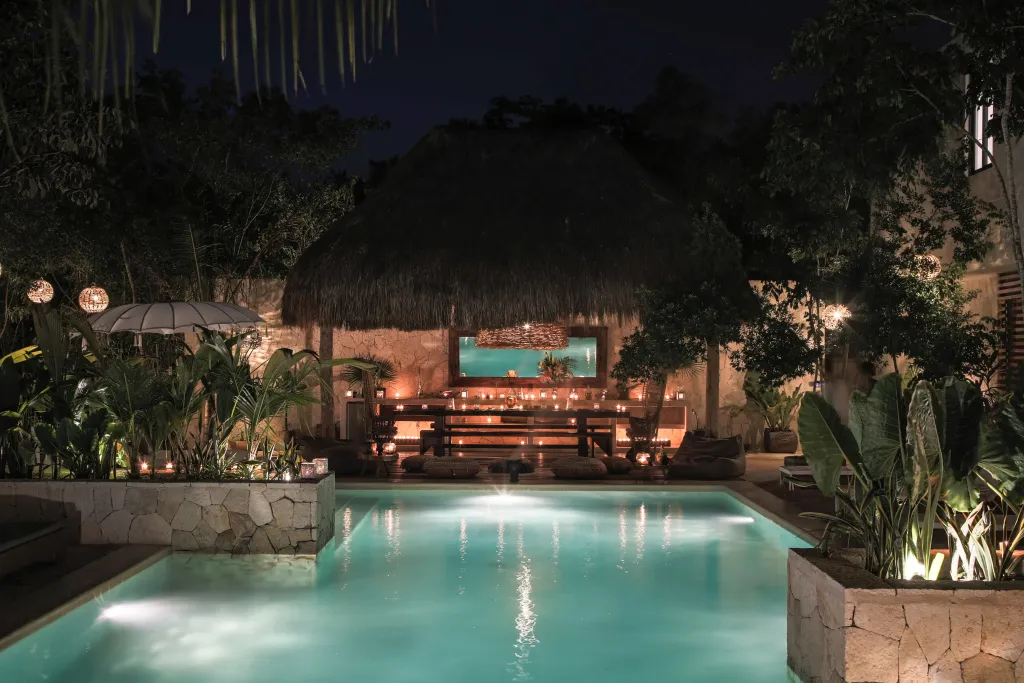 Piscine illuminée avec un espace de détente ombragé en arrière-plan.