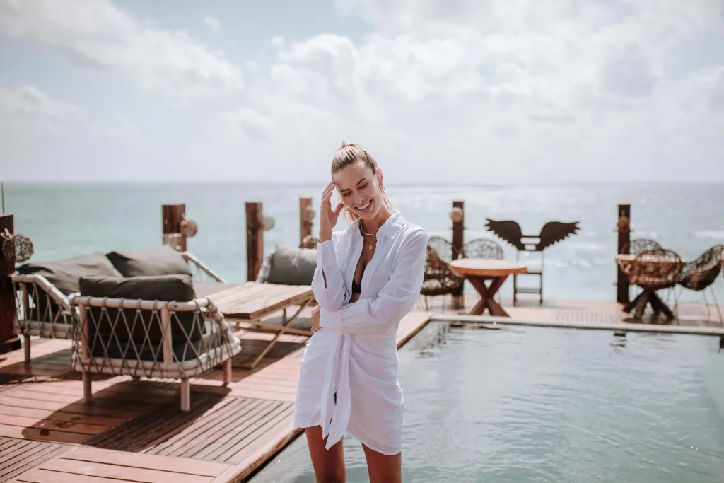 Une jeune femme souriante se tient près d'une piscine à débordement avec vue sur la mer.