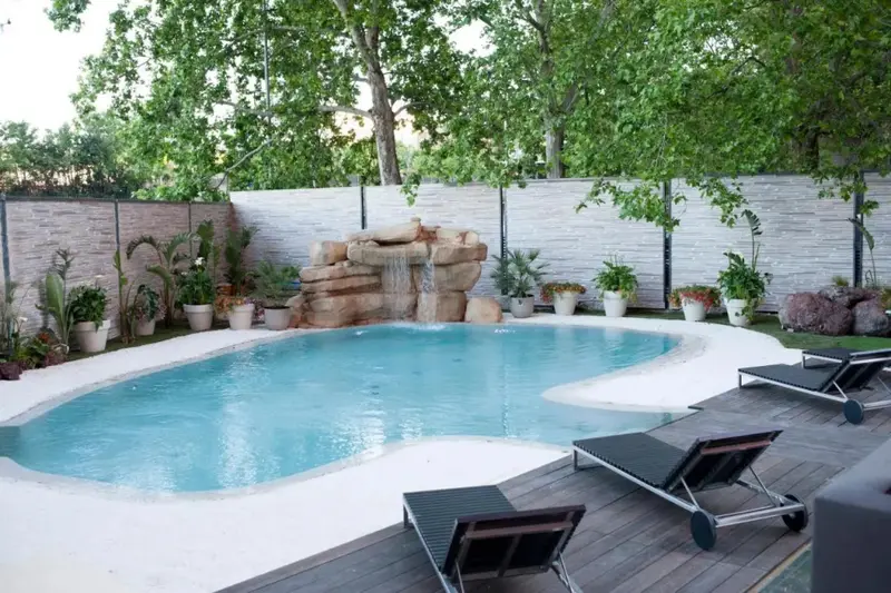 Une piscine avec une cascade rocheuse et des transats sur une terrasse.
