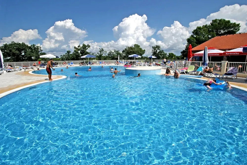 Une piscine ensoleillée avec des personnes se baignant et se relaxant au bord.