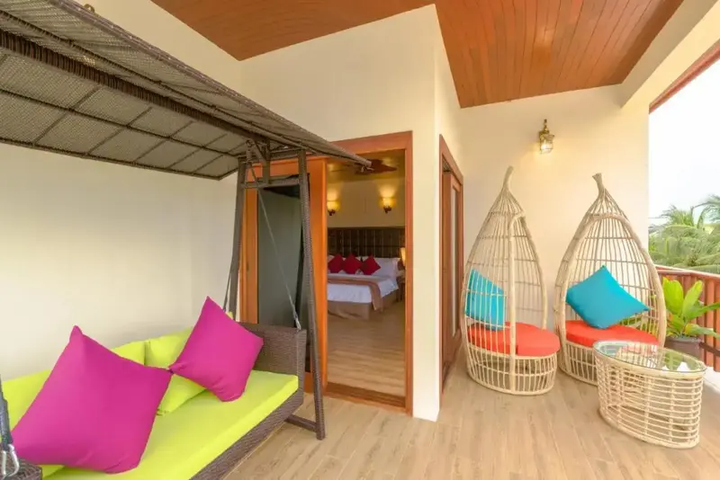 Espace de détente extérieur avec canapé et fauteuils suspendus donnant sur une chambre.