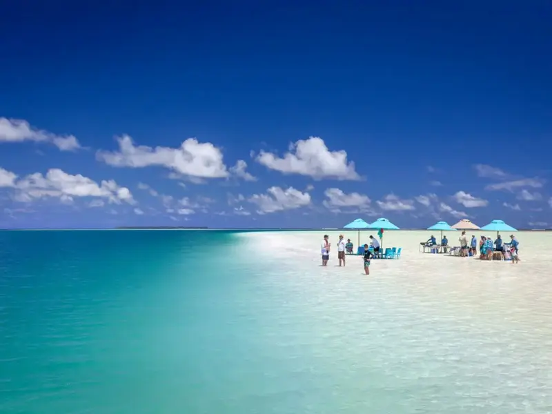 Plage de sable blanc avec parasols et quelques personnes.