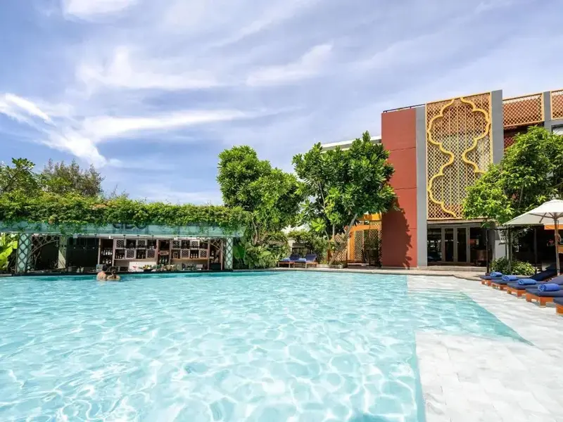 Une piscine turquoise bordée de transats sous des parasols, avec un bar ombragé en arrière-plan.