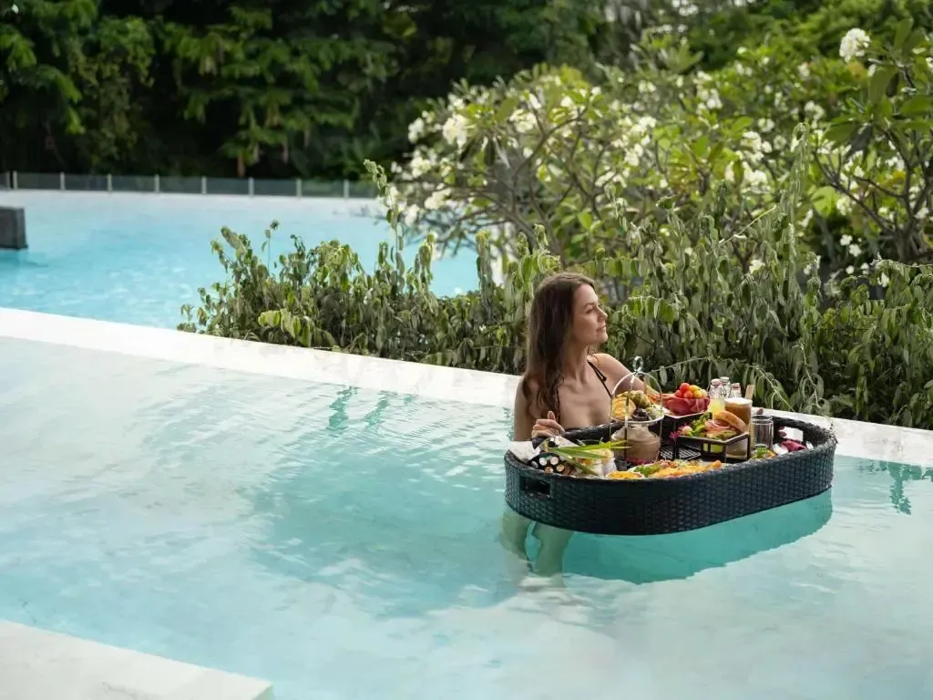 Une femme se détend dans une piscine avec un plateau de nourriture flottant à côté d'elle.