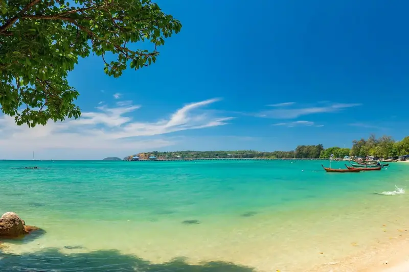 Une plage de sable blanc bordée d'une eau turquoise sous un ciel bleu.