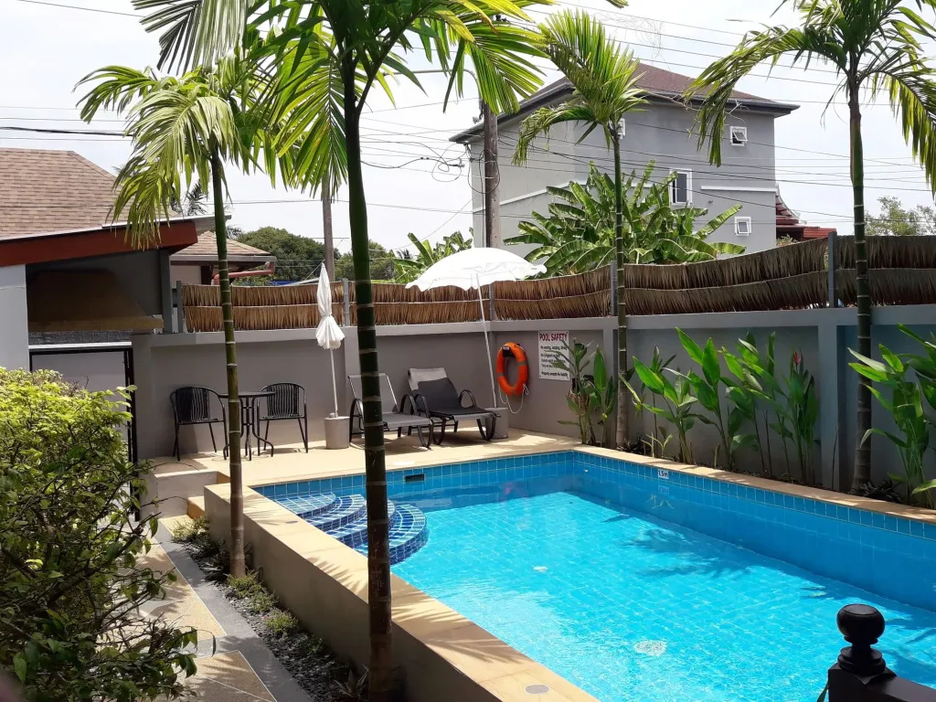 Une piscine rectangulaire entourée d'une terrasse avec des chaises longues et de la végétation tropicale.