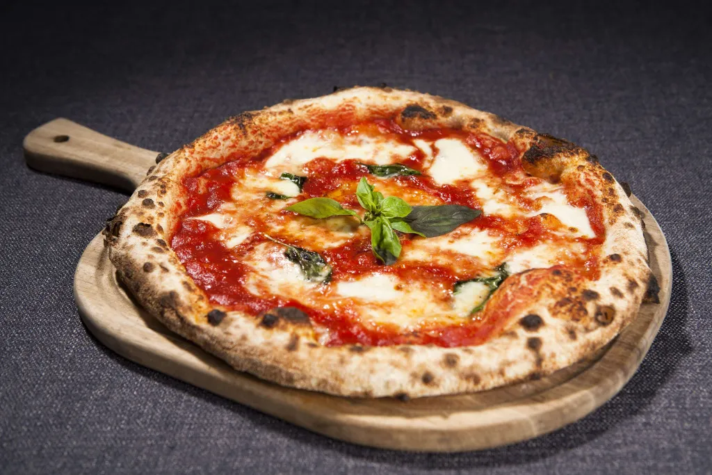 Une pizza à la tomate et à la mozzarella fraîche est présentée sur une planche à pain.