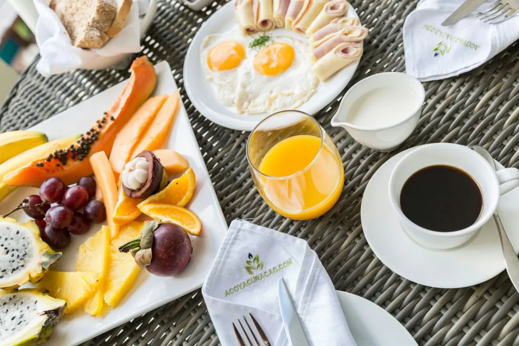 Une table est dressée avec un petit-déjeuner copieux composé de fruits frais, d'œufs, de jambon et de viennoiseries.