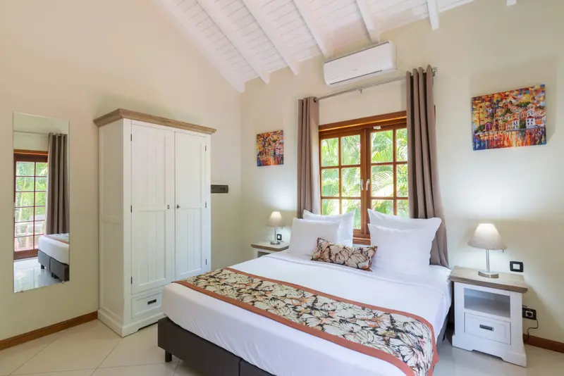 Une chambre lumineuse avec un grand lit et une fenêtre donnant sur la végétation.