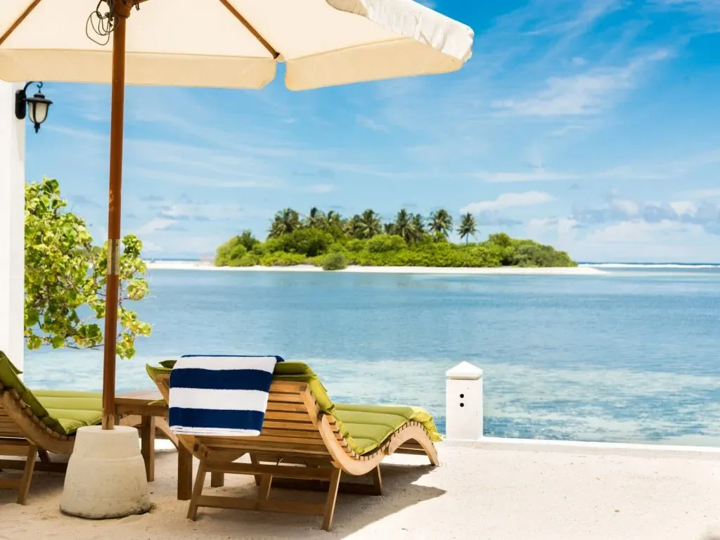 Transats et parasol sur une plage de sable blanc face à une île tropicale.