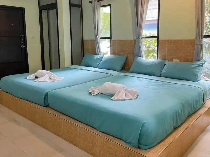 Deux lits jumeaux turquoise dans une chambre lumineuse avec des oreillers et des serviettes décoratives.